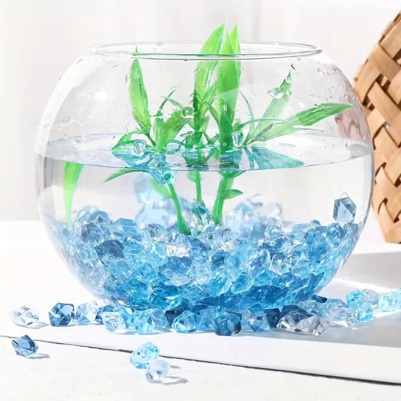 A glass bowl filled with blue acrylic pebbles and green plants.