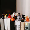 A collection of twelve mini resin Halloween duck figurines in various colors and designs displayed on a shelf.