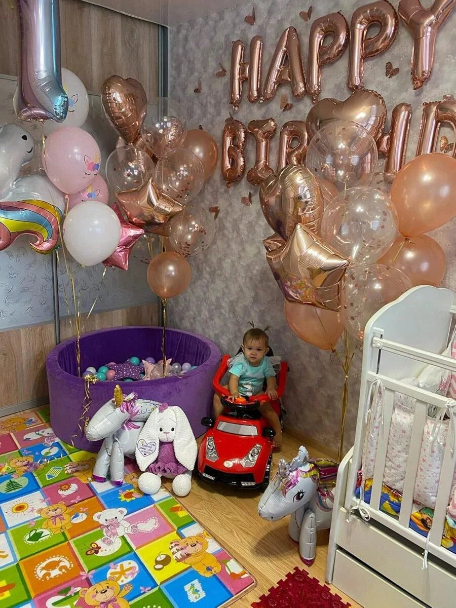A colorful room decorated with rose gold and pink balloons, including foil and latex balloons, next to a baby and a white cri