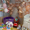 A colorful room decorated with rose gold and pink balloons, including foil and latex balloons, and a small child sitting in a