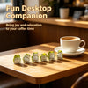 A set of six cute mini resin frog figurines sitting on a wooden table next to a cup of coffee.