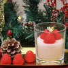 A glass jar filled with white wax and topped with fresh strawberries, set against a festive Christmas tree backdrop.