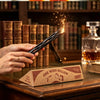 A hand holds a wishing willow stick with a box on a wooden surface, set against a backdrop of bookshelves.