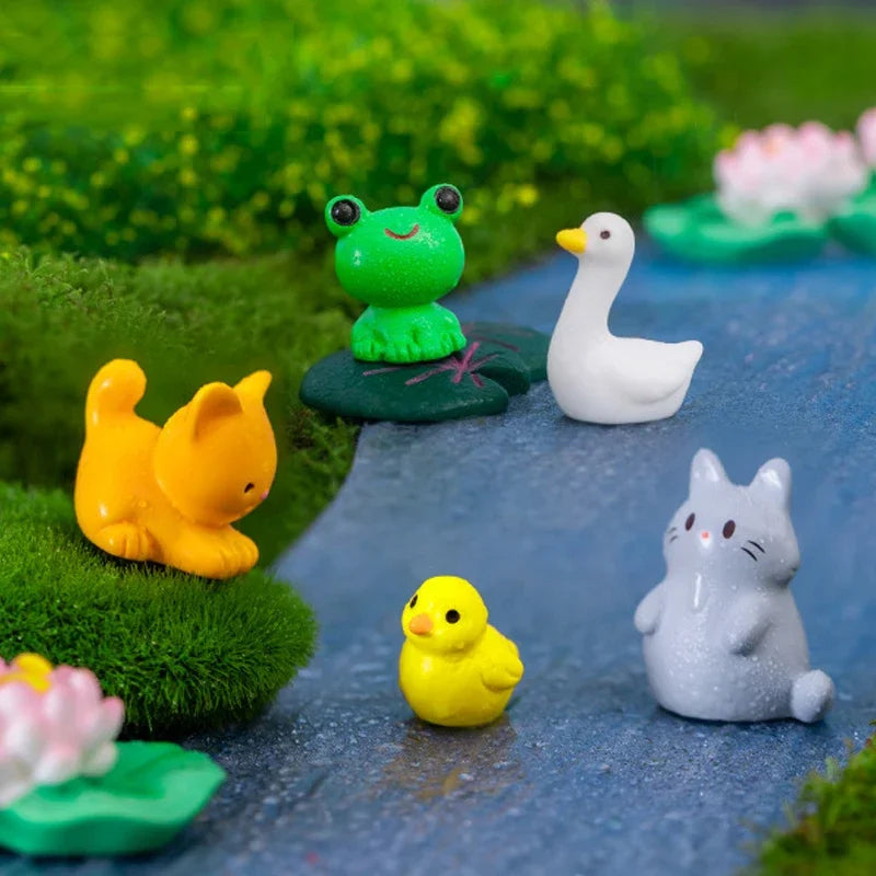 A collection of small, colorful animal figurines including a frog, a duck, a goose, a cat, and a chick arranged on a blue sur