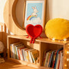 A wooden shelf displays a red heart-shaped ornament and several books, next to a framed picture of a rabbit and a yellow cush