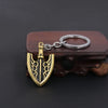 A gold-colored arrow metal keychain with a black design is resting on a dark brown wooden surface.