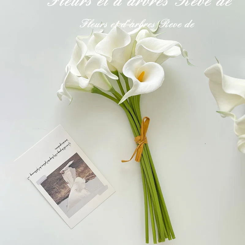 A bouquet of six white artificial calla lilies with green stems and natural light background.