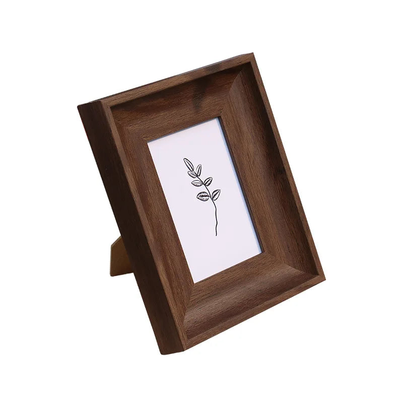 A dark brown wooden photo frame with a white mat displaying a simple line drawing of a leafy branch.