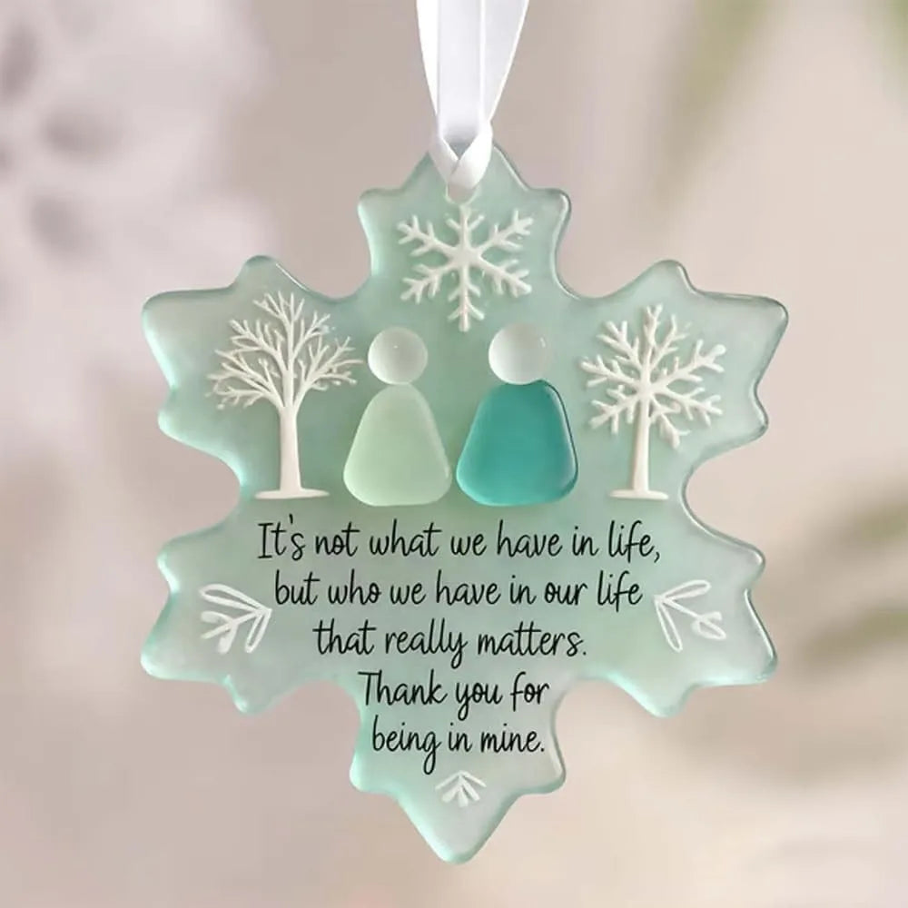 A teal snowflake sea glass ornament with a silhouette of two people inside, hanging by a white string.