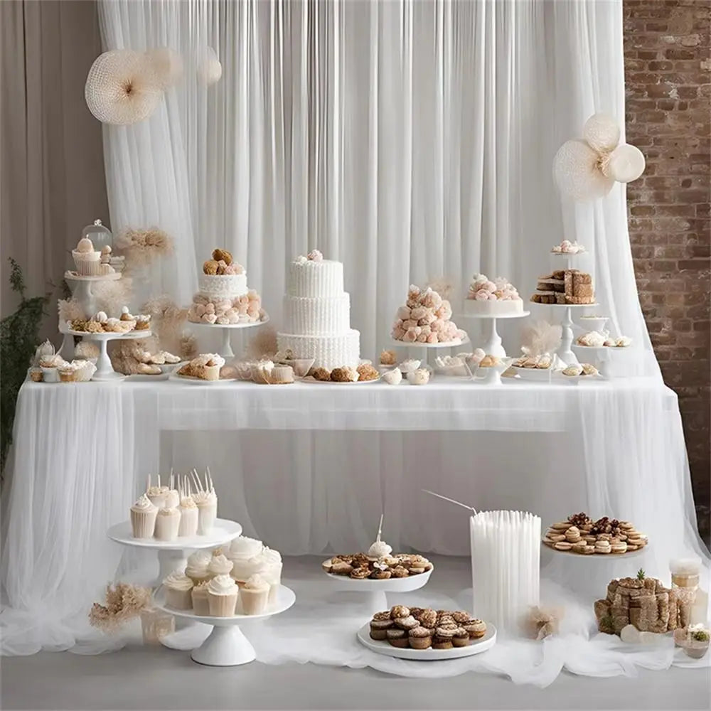 A white tiered cake display on a table decorated with sheer tulle fabric and dried floral elements.