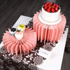 A pink tiered cake display featuring a main cake and five small cupcakes on a decorative stand.