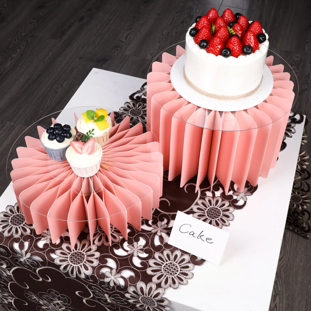 A pink tiered cake display featuring a main cake and five small cupcakes on a decorative stand.