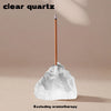 A clear quartz point rests on a rough, translucent stone with a wooden stick, excluding aromatherapy.