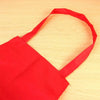 A bright red waterproof kitchen apron with a shoulder strap is shown lying on a light wooden surface.