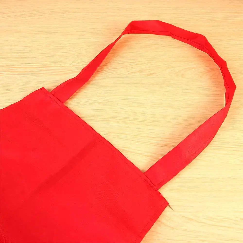A bright red waterproof kitchen apron with a shoulder strap is shown lying on a light wooden surface.