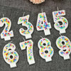 Glitter number birthday candles in pink and white with candy beads arranged on a dark gray surface.