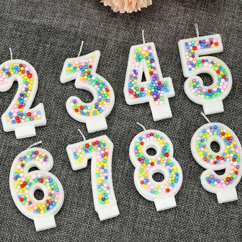 Glitter number birthday candles in pink and white with candy beads arranged on a dark gray surface.