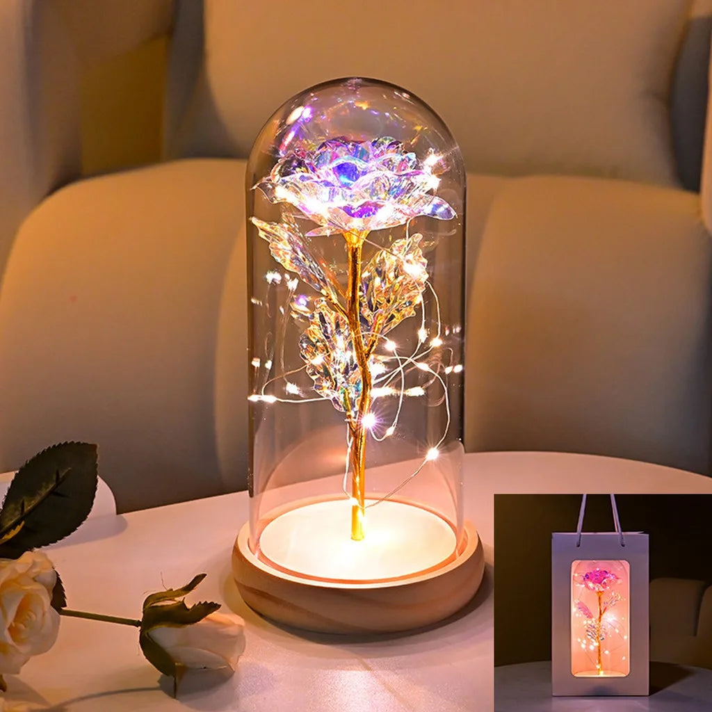 An LED galaxy rose artificial flower displayed inside a glass dome on a wooden base.