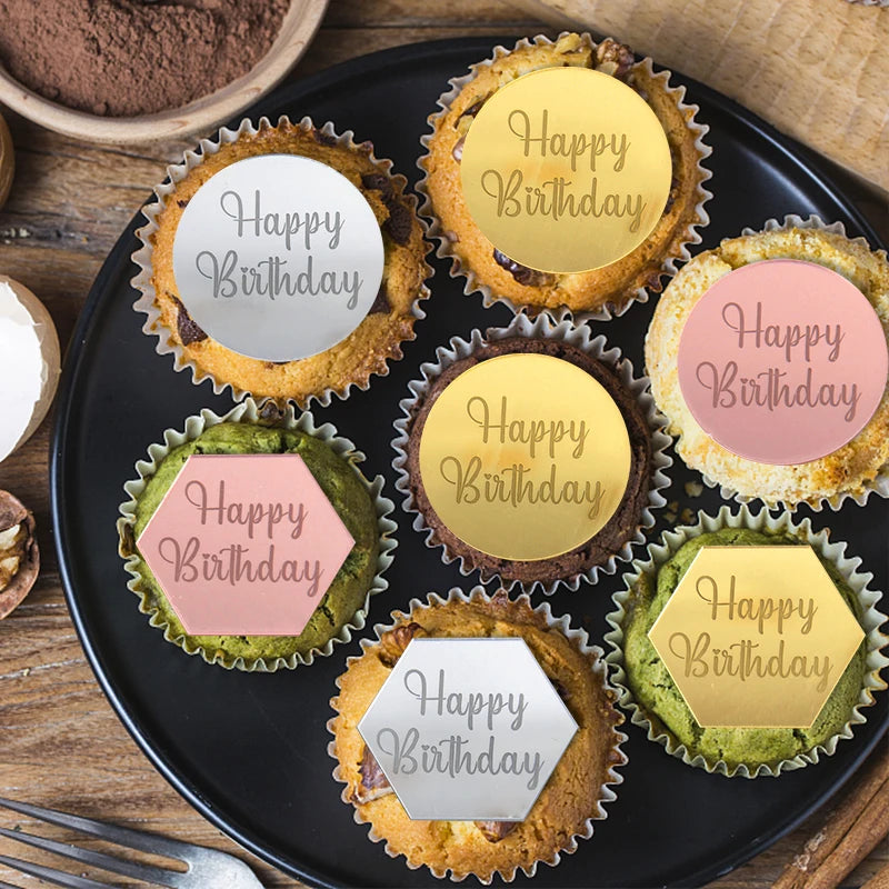 A black platter holds ten cupcakes with gold and pink birthday message toppers.