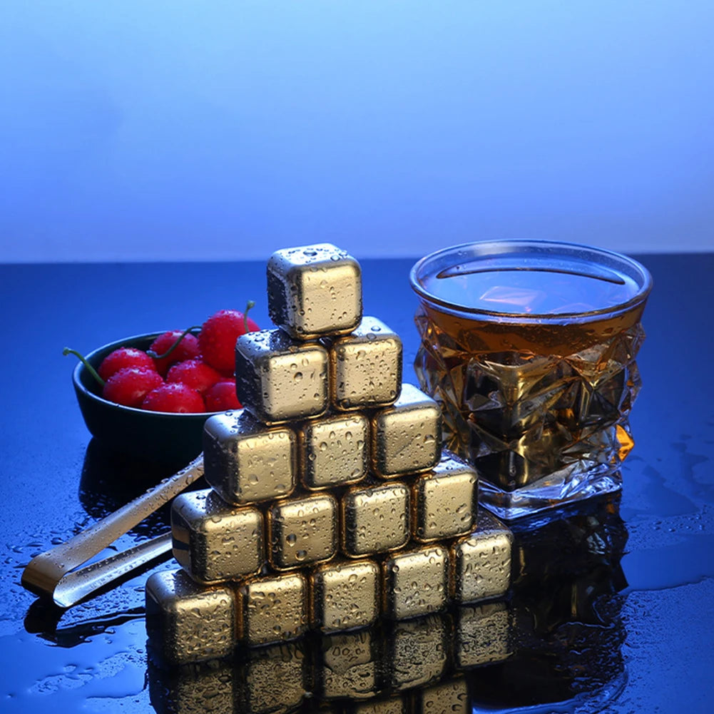 A stack of reusable stainless steel ice cubes on a dark surface next to a glass of amber liquid.