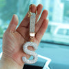 A hand holds a crystal letter keychain charm with a gold ring and a sparkling letter S.