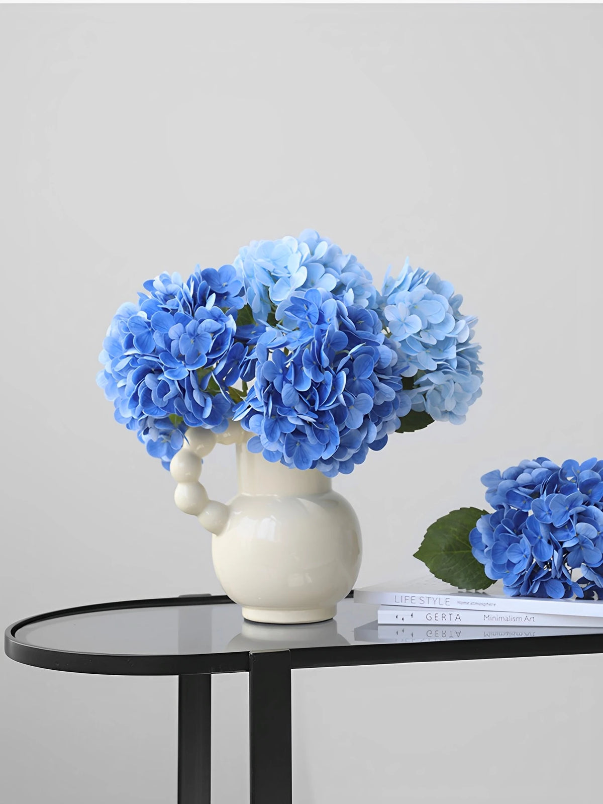 A bouquet of bright blue artificial hydrangea flowers in a white vase on a black table.