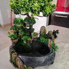A resin waterfall desktop fountain featuring lush green foliage and rocks with LED lighting.
