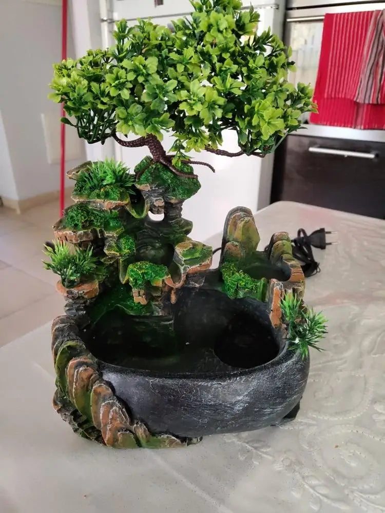 A resin waterfall desktop fountain featuring lush green foliage and rocks with LED lighting.