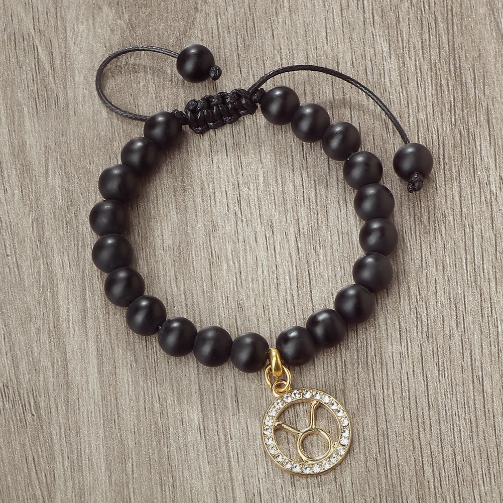 A handmade beaded bracelet featuring natural black stones and a gold zodiac charm.
