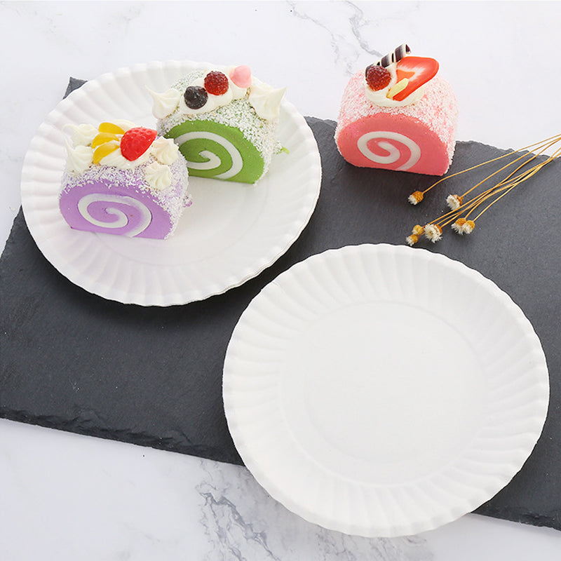 Three colorful rolled desserts on white plates and a dark slate board.