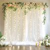 Elegant white wedding tulle backdrop decorated with floral greenery and twinkling string lights.