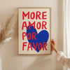 A framed canvas print with the text MORE AMOR FOR FAVOR in bold red and blue lettering on a light background.