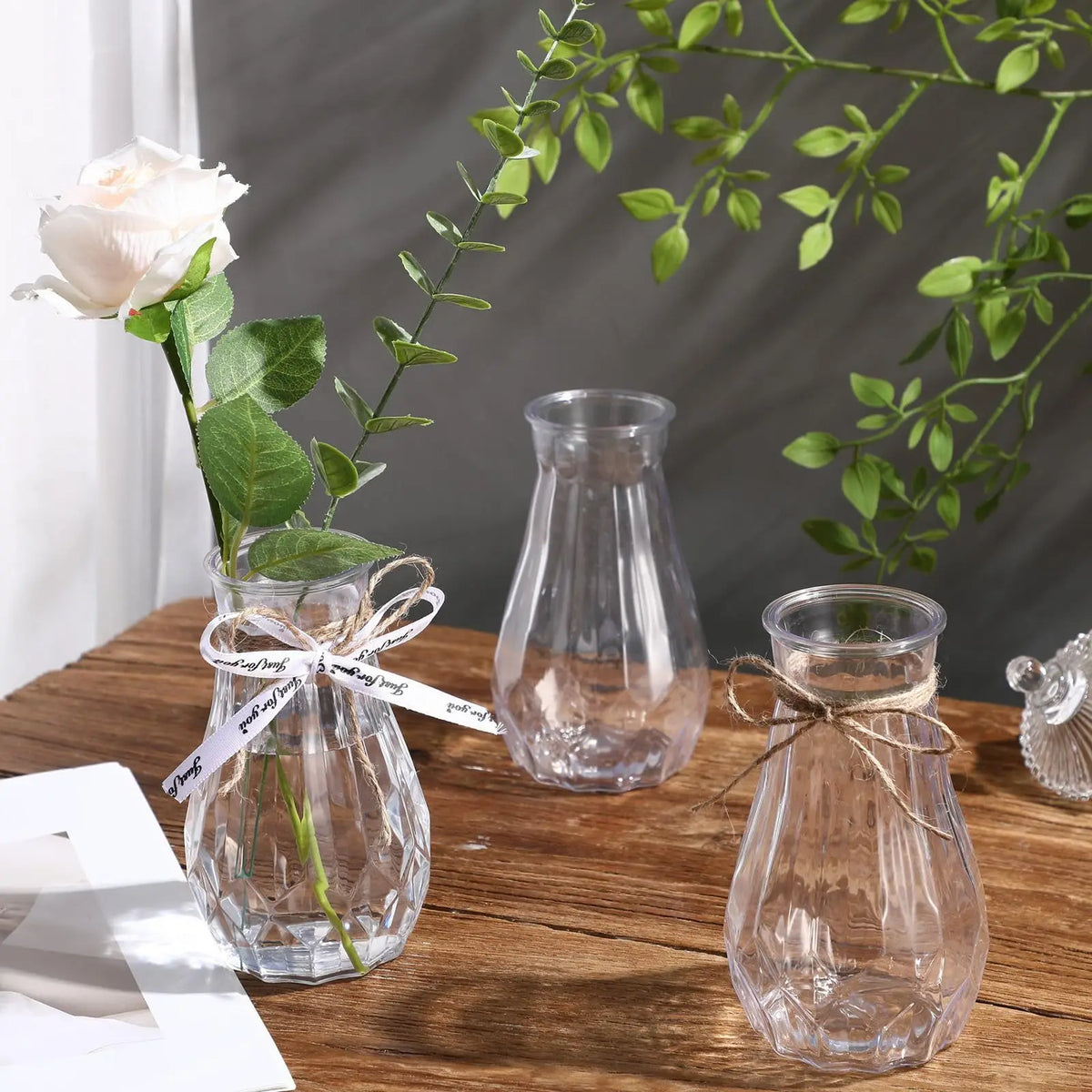 Clear faceted diamond crystal vase holding a light pink rose and green foliage on a wooden table.