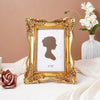 A gold-framed photo frame with a white mat displaying a silhouette of a woman on a light pink background.