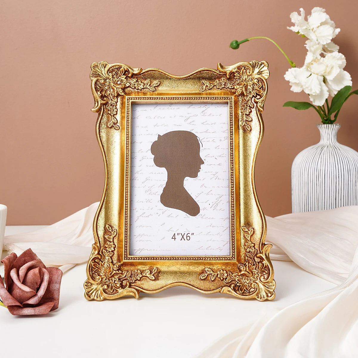 A gold-framed photo frame with a white mat displaying a silhouette of a woman on a light pink background.