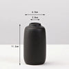 A matte black ceramic vase with a cylindrical shape and a narrow opening, shown against a white background.