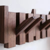 A dark brown wooden piano key wall coat rack with eight angled hooks mounted on a white wall.