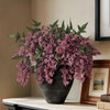 A large arrangement of artificial nandina berry stems in dusty plum color displayed in a dark vase on a mantelpiece.