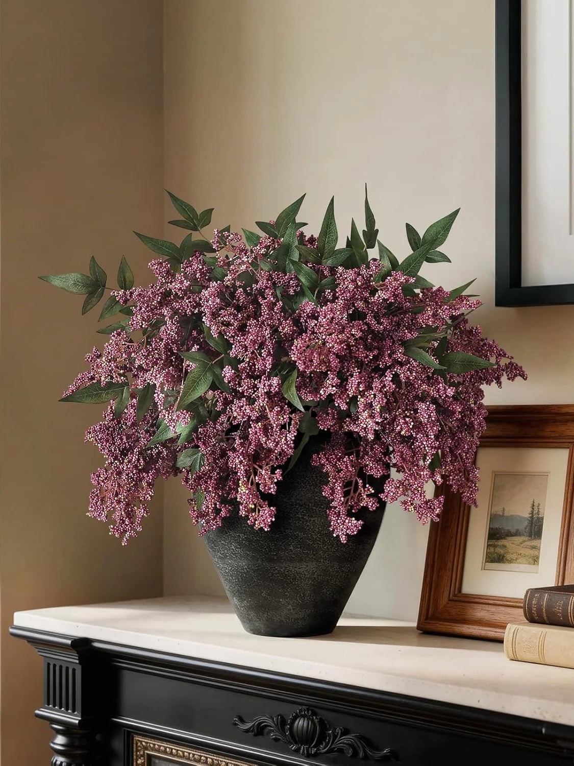 A large arrangement of artificial nandina berry stems in dusty plum color displayed in a dark vase on a mantelpiece.