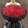 A bouquet of red silk roses wrapped in black paper and tulle fabric.