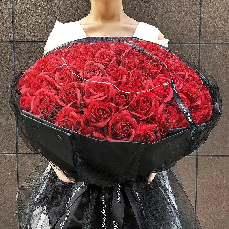 A bouquet of red silk roses wrapped in black paper and tulle fabric.