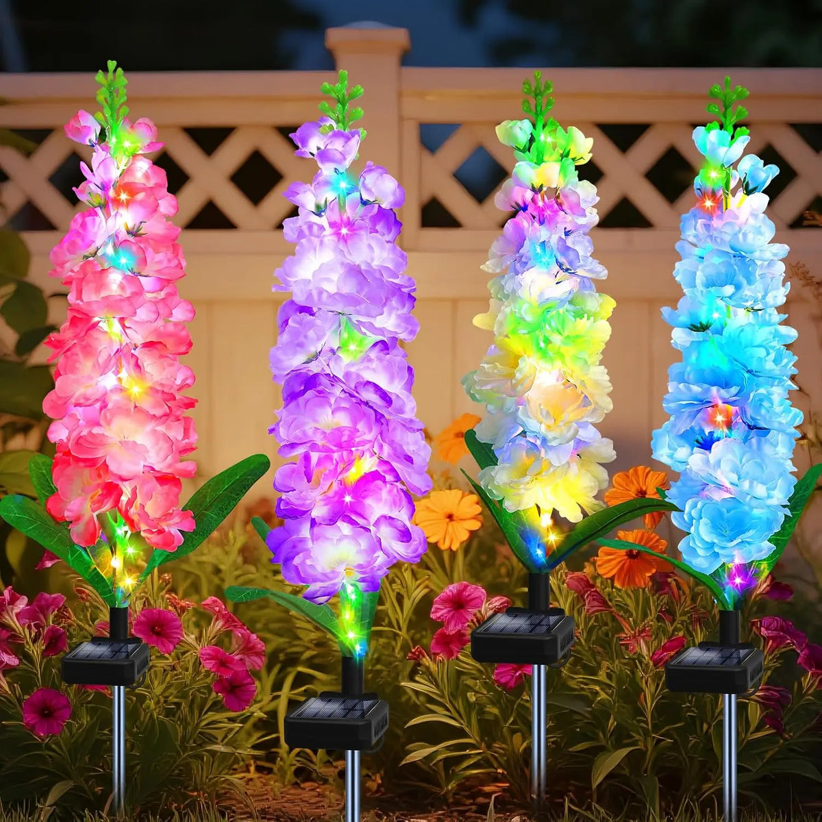 Four vertical solar-powered lights illuminate vibrant pink, purple, yellow, and blue delphinium flowers in a garden setting.