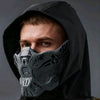A man wearing a tactical silicone half-face mask under a black hood.