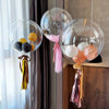 Clear balloons filled with confetti and tissue paper in shades of yellow, black, pink, and peach hanging by strings