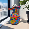 A colorful resin figurine shaped like a frog with large eyes sitting on a windowsill.