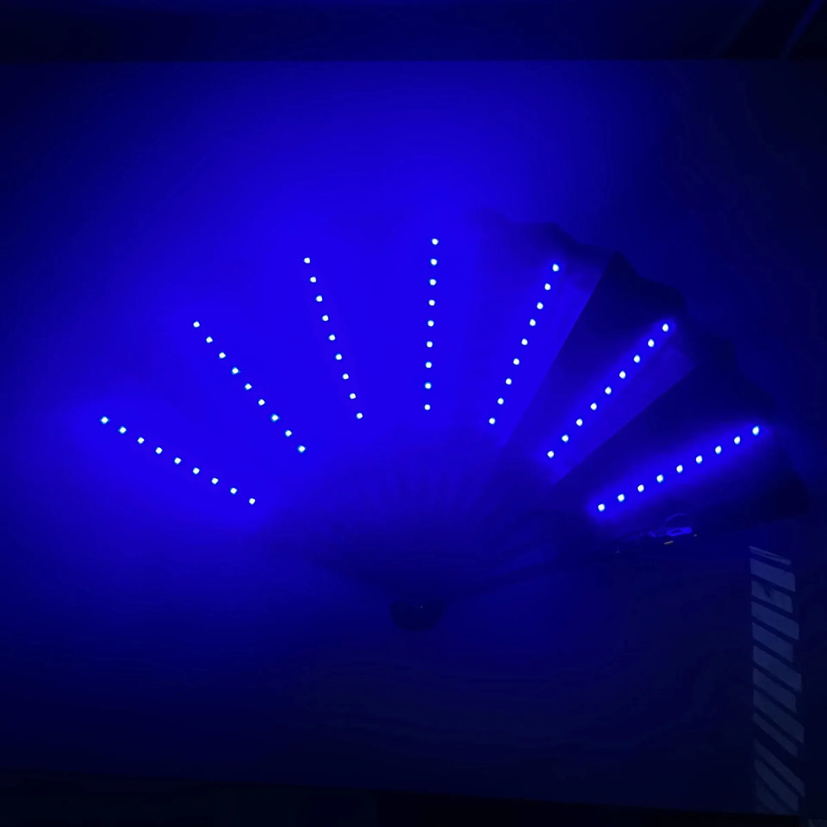 A folding hand fan illuminated by bright blue LED lights, showing a radial pattern of illumination.