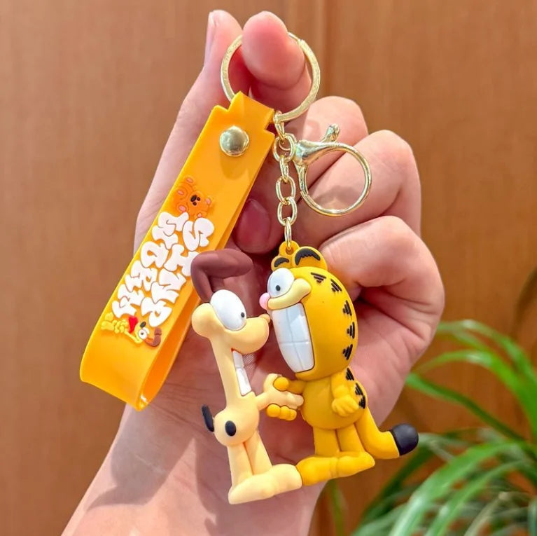 A hand holds a yellow Garfield cartoon keychain pendant attached to an orange tag.