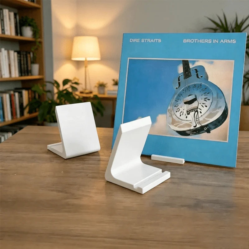 A white minimalist vinyl record and CD display stand sits on a wooden table next to a blue book.