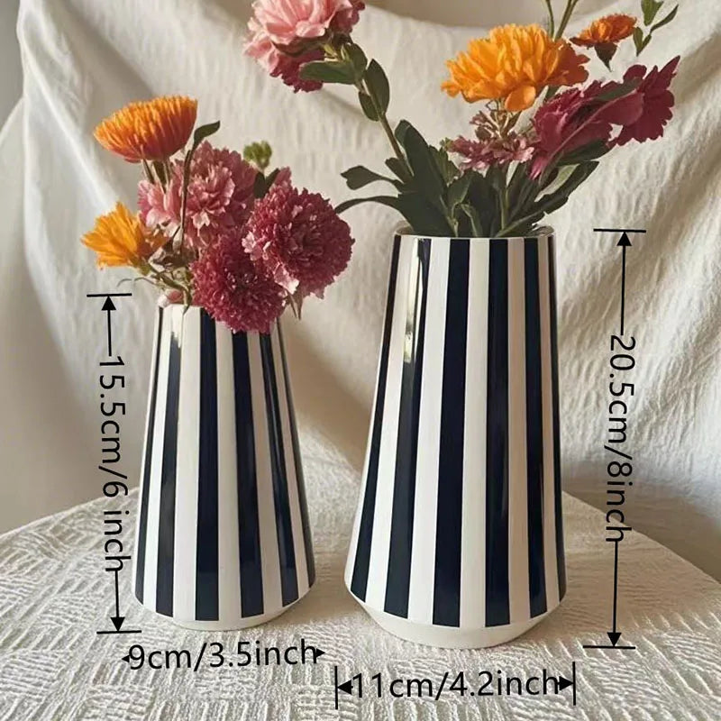 A ceramic vase with black and white vertical stripes holds a bouquet of pink and orange flowers.