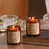 Two amber glass candles in jars with labels reminding the viewer that they love you and their butt is perfect